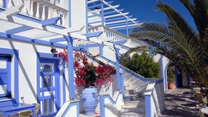 A white building with blue accents, a staircase, and outdoor seating. - Stavros Villas (Santorini)