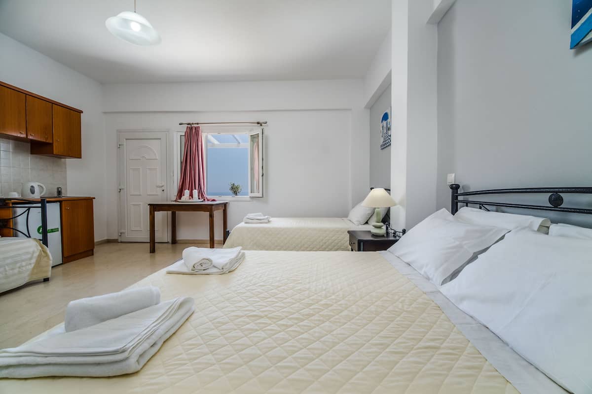 A hotel room with two beds, a desk, a chair, a window with curtains, and a view of the sea.