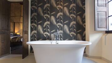 A modern bathroom with a freestanding bathtub, a wooden door leading to another room, and a patterned wallpaper.