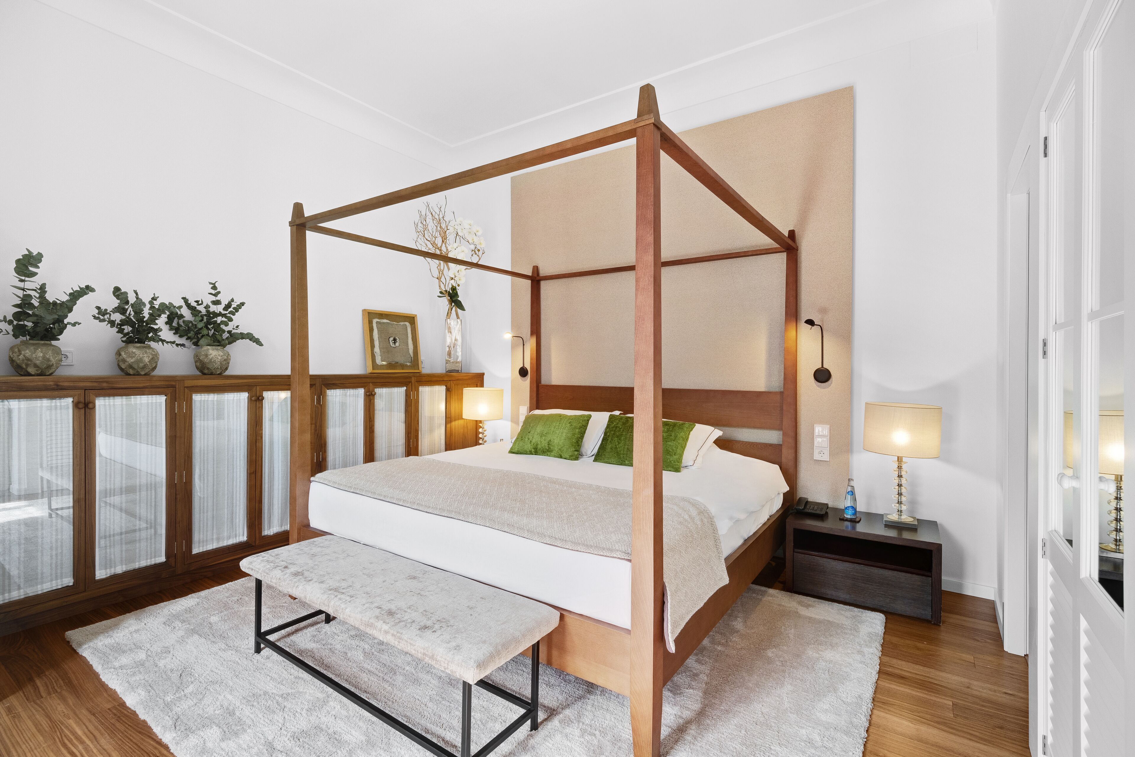 A four-poster bed with a bench, bedside tables, and potted plants.