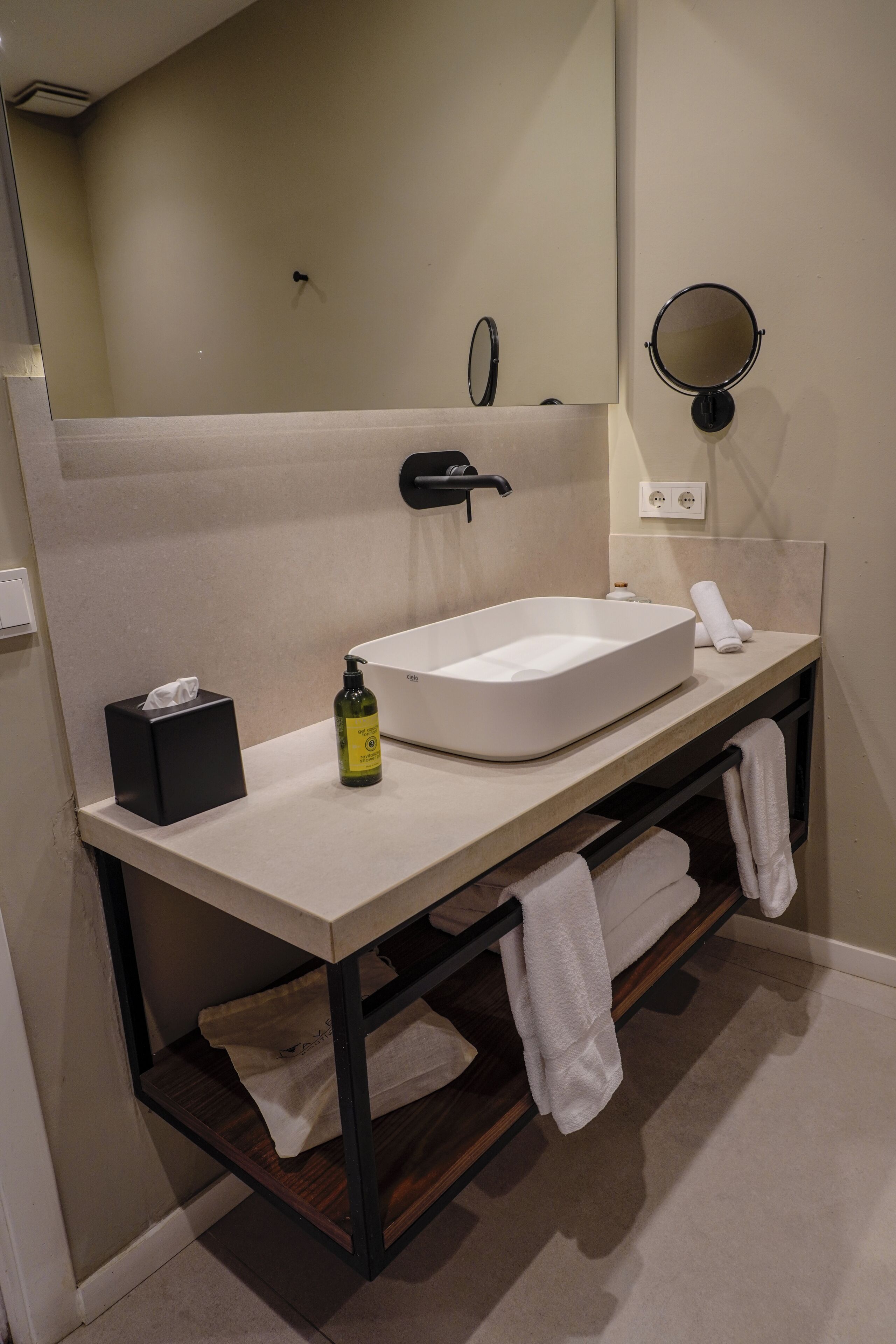 A modern bathroom with a rectangular sink, a mirror, a towel rack, and a tissue box.