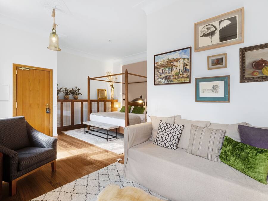 A modern living room with a wooden floor, a sofa, a chair, and a four-poster bed.