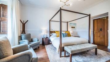 A bedroom with a four-poster bed, a sofa, a bedside table, and a nightstand.