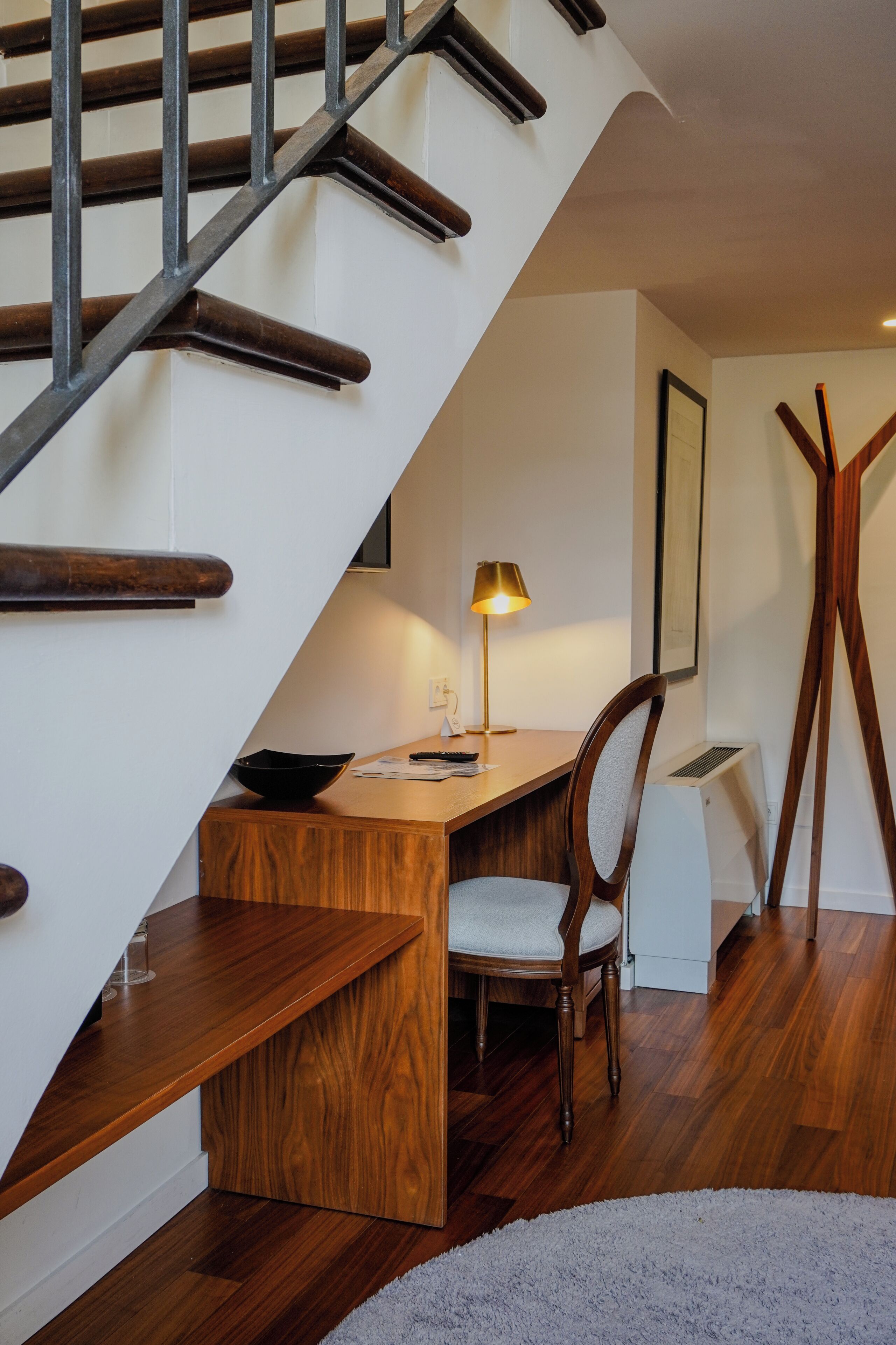 A staircase with wooden steps and metal railings, a desk with a chair, a lamp, and a framed picture on the wall.