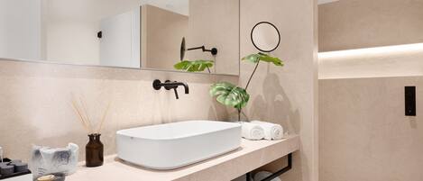 Un baño moderno con un espejo grande, un lavabo blanco, una planta y toallas dobladas con cuidado.