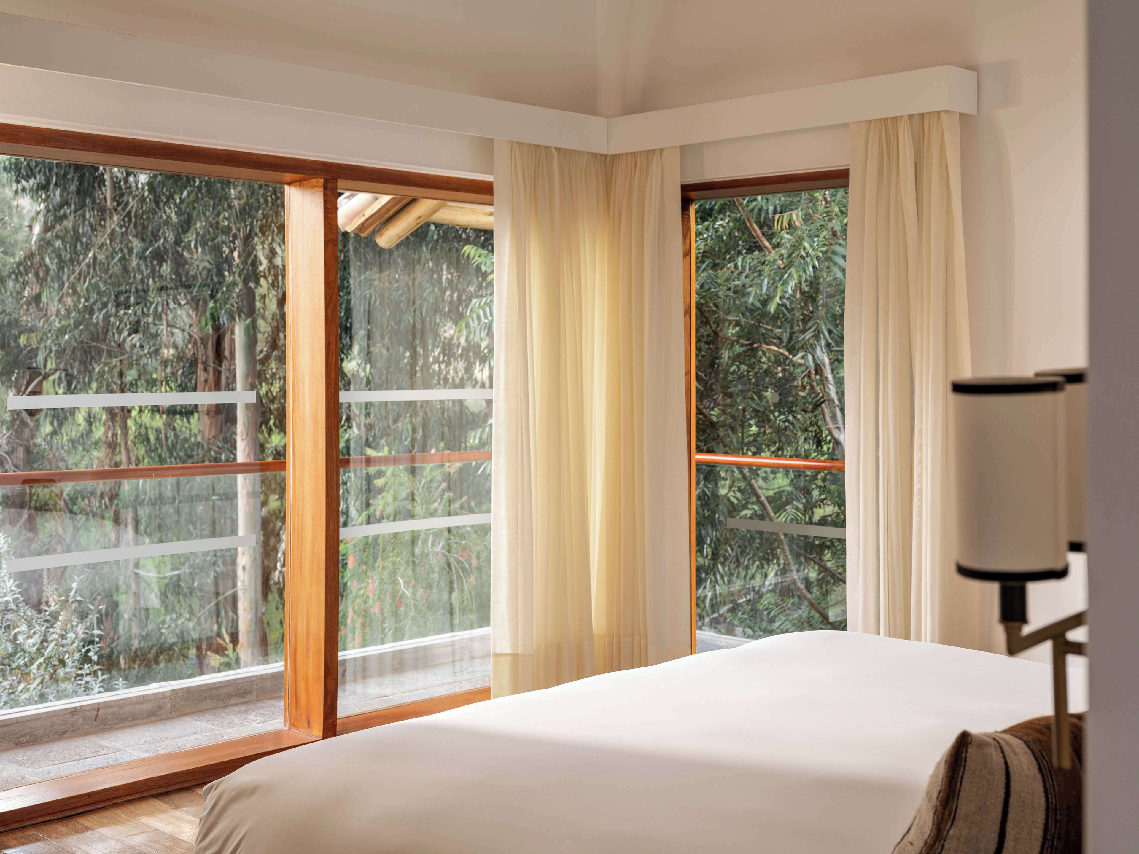 A bedroom with a large bed, a window with curtains, and a view of greenery outside.