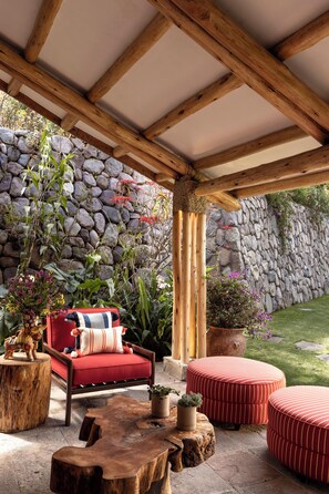 Un patio couvert doté d’un mur en pierre, de poutres en bois, d’un canapé rouge et de poufs ronds.