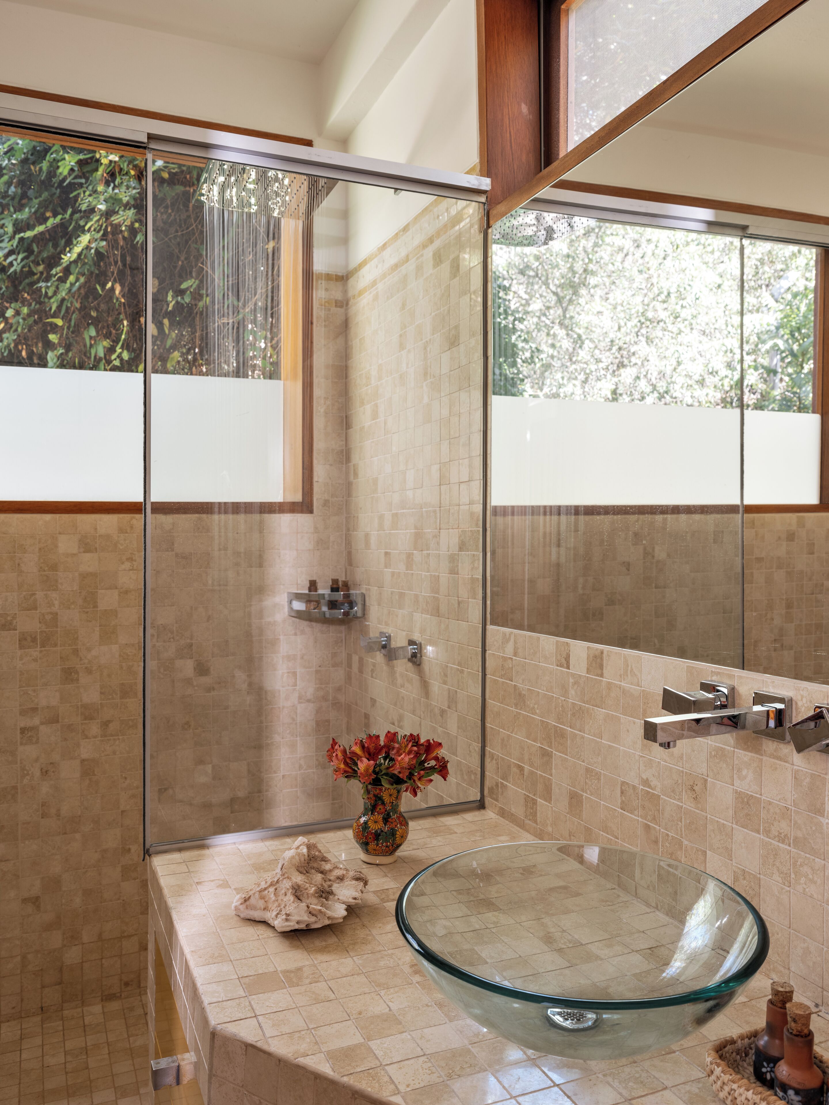 A modern bathroom with a glass bowl sink, a shower enclosure, and a large mirror.