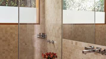 A modern bathroom with a glass bowl sink, a shower enclosure, and a large mirror.
