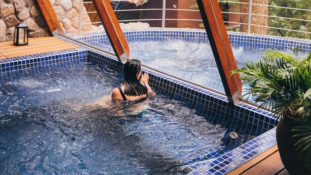 A person in a hot tub with a stone wall and a tiled roof in the background. - Rio Sagrado, A Belmond Hotel, Sacred Valley (Urubamba)