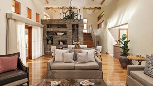 A spacious living room with a high ceiling, a fireplace, a staircase, and a large window. - Rio Sagrado, A Belmond Hotel, Sacred Valley (Urubamba)