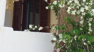 A white building with a wooden balcony and a window with brown shutters.