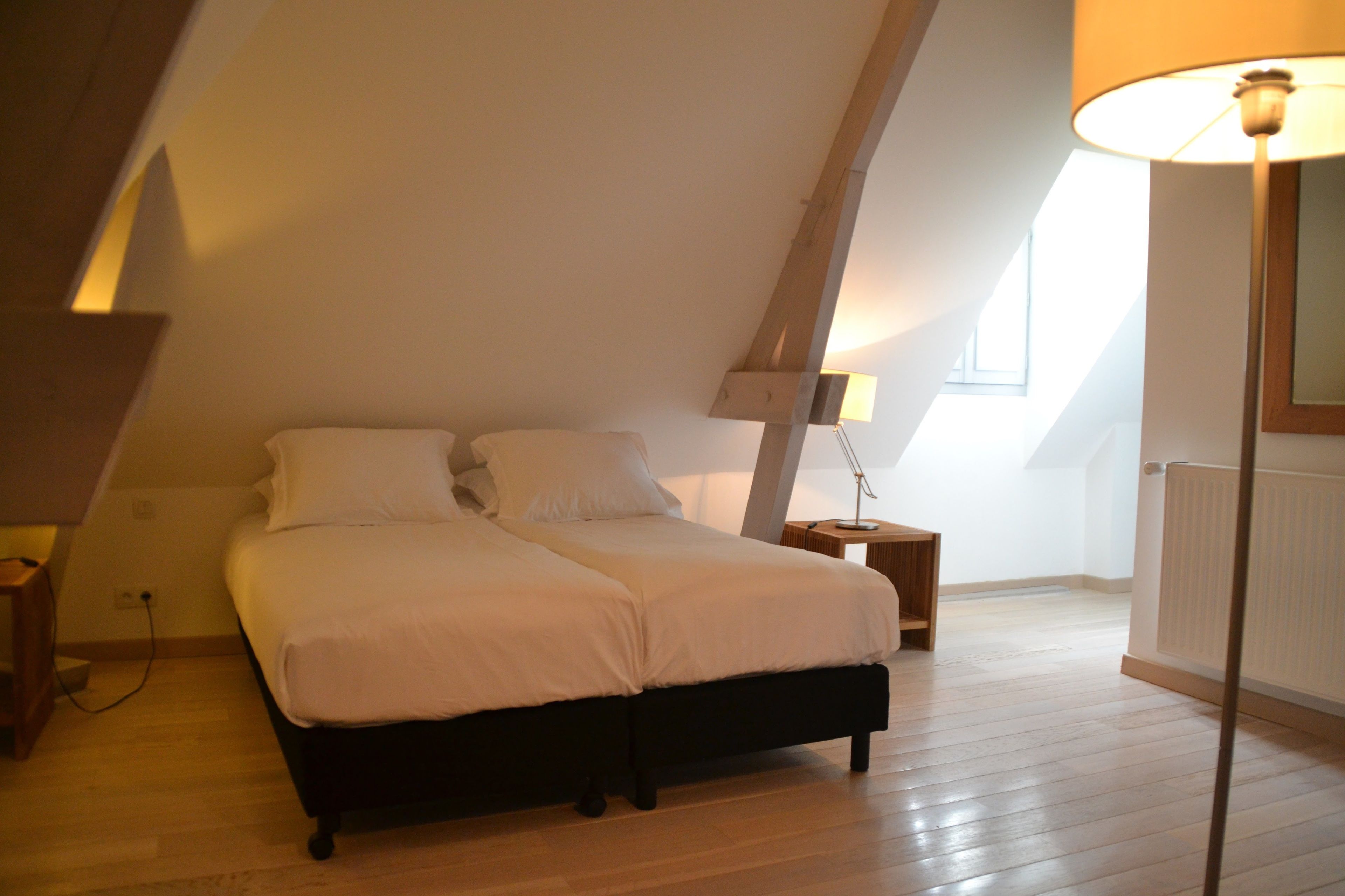 A bedroom with a sloped ceiling, a double bed, a bedside table, and a floor lamp.