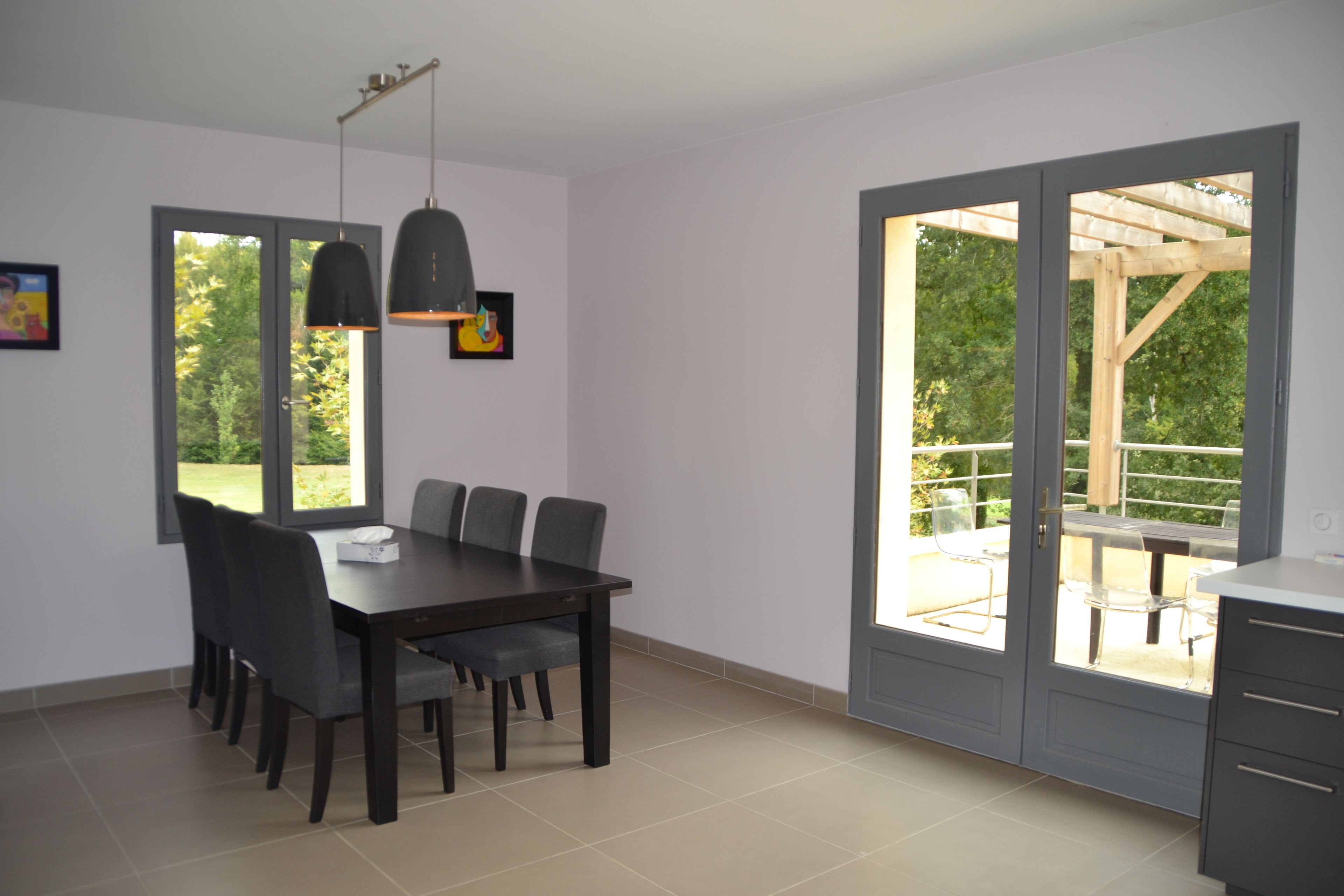 Un comedor con una mesa y sillas, una lámpara colgante y vistas a un patio exterior a través de un ventanal.