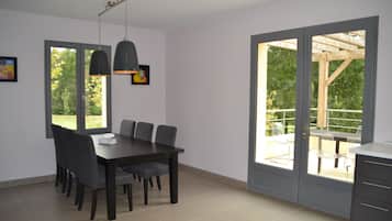 Un comedor con una mesa y sillas, una lámpara colgante y vistas a un patio exterior a través de un ventanal.