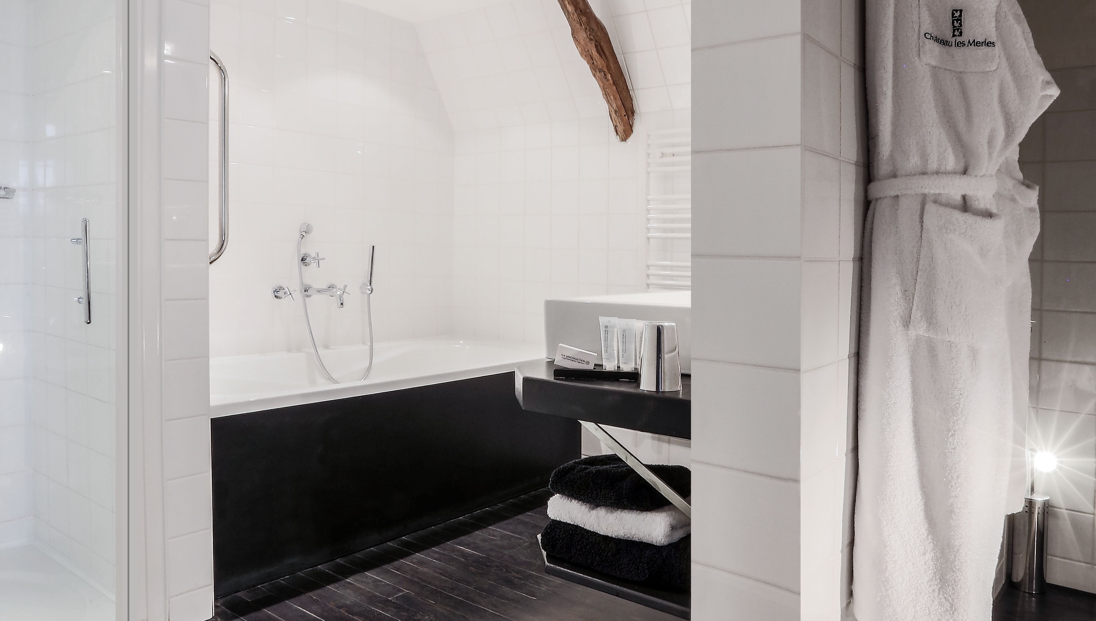 Casa de banho moderna com chuveiro de vidro, banheira preta e toucador branco com artigos de higiene pessoal.