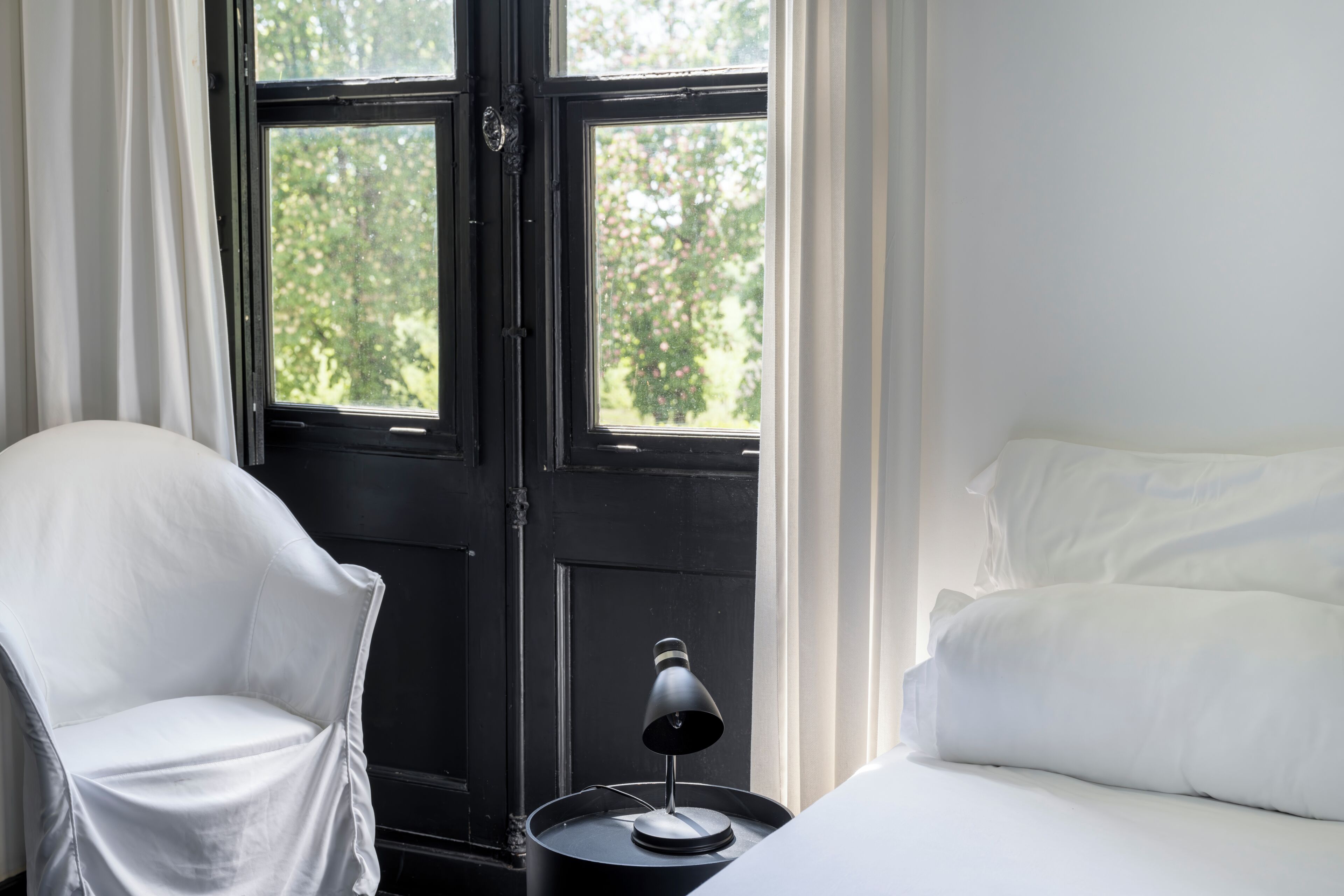 Une pièce comprenant un lit, une chaise, une lampe et une fenêtre donnant sur un paysage verdoyant.