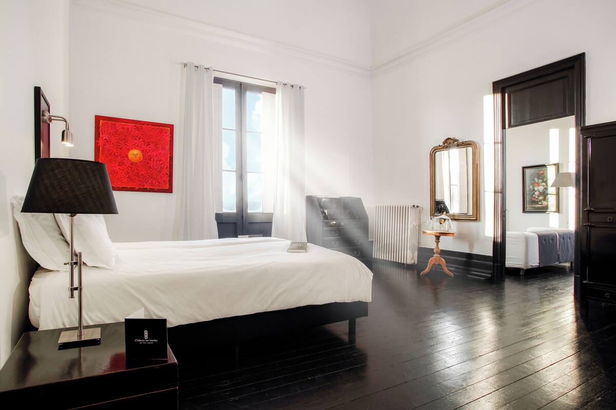 Habitació d'hotel amb un llit, una taula de treball amb una làmpada, un radiador i un mirall gran.