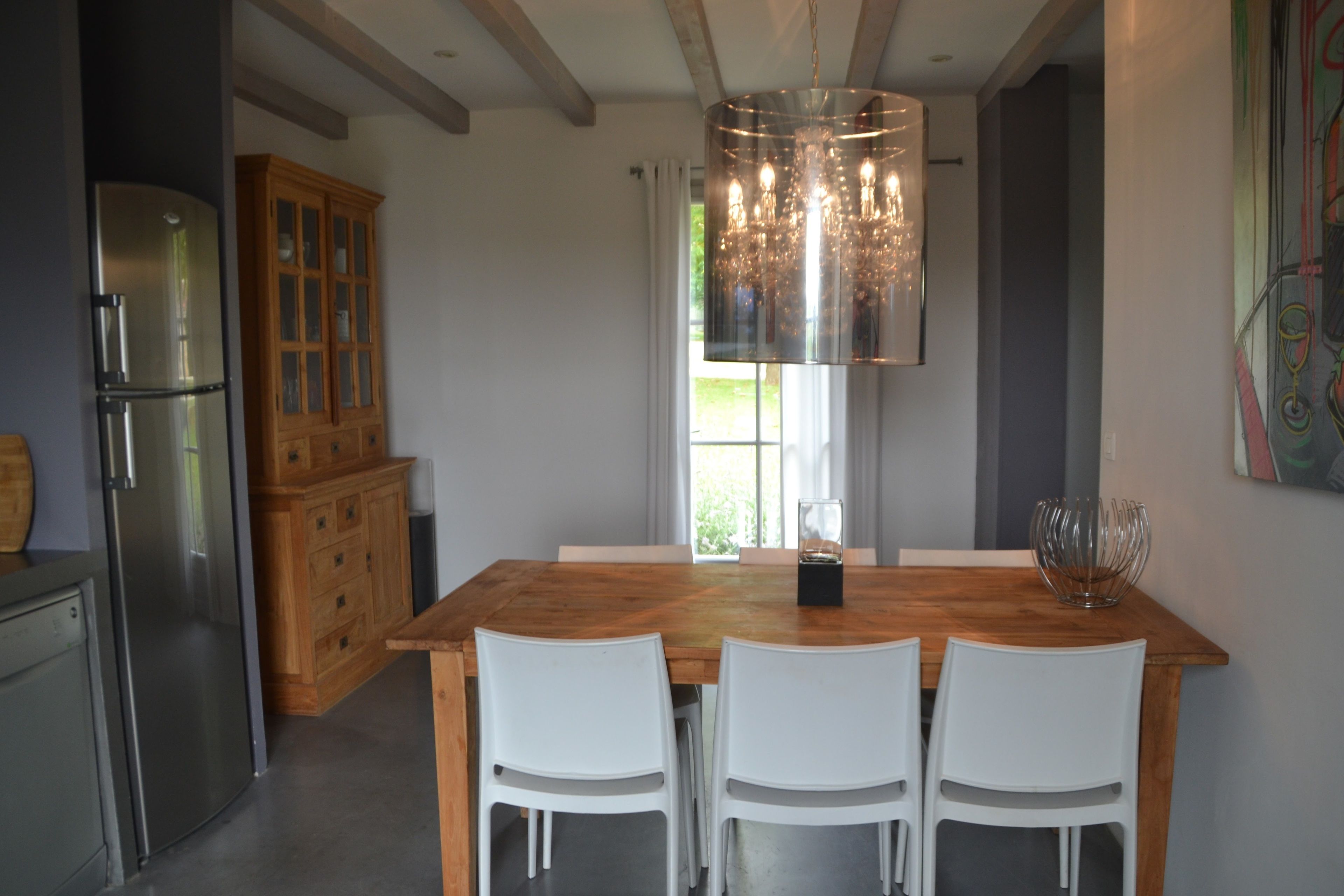 A modern kitchen with a wooden dining table, white chairs, a stainless steel refrigerator, and a wooden cabinet.