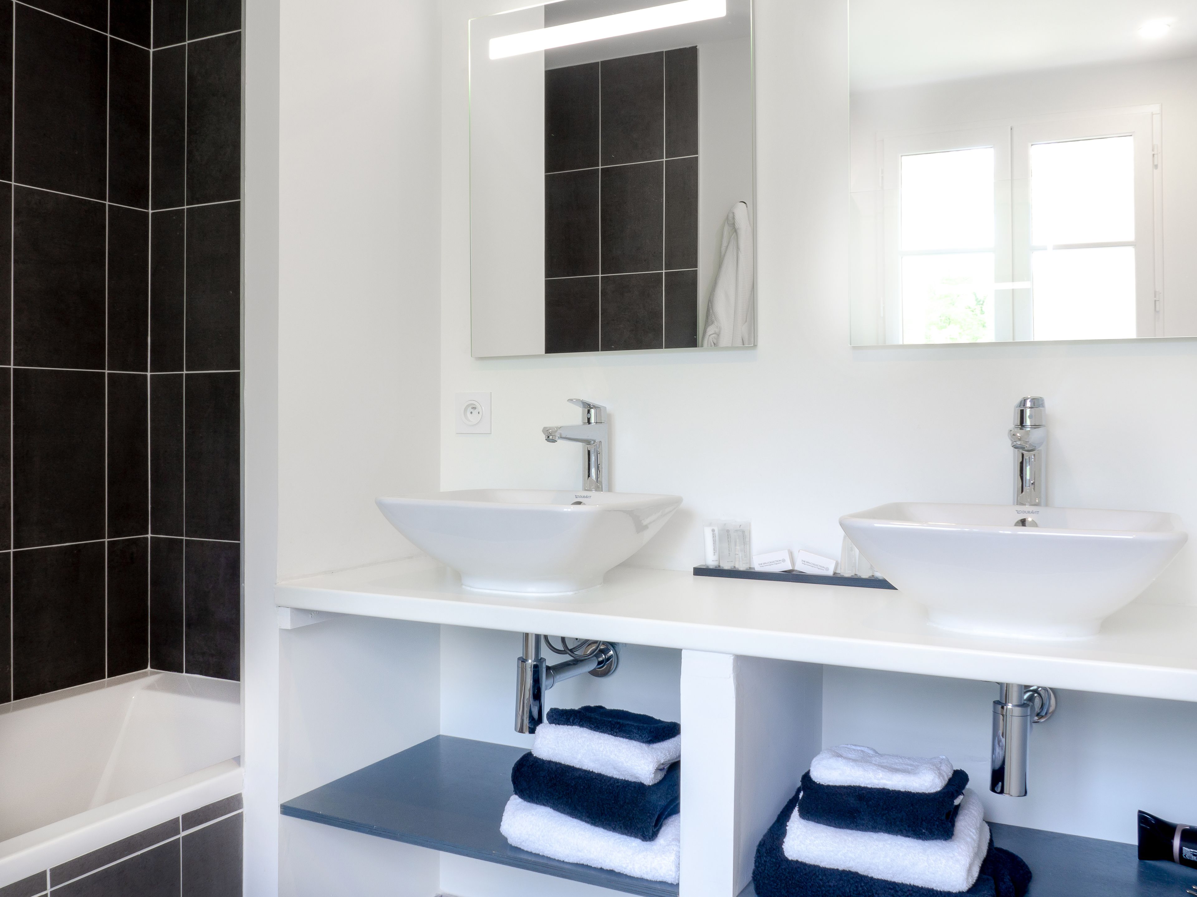 A modern bathroom with two sinks, a large mirror, and a bathtub.