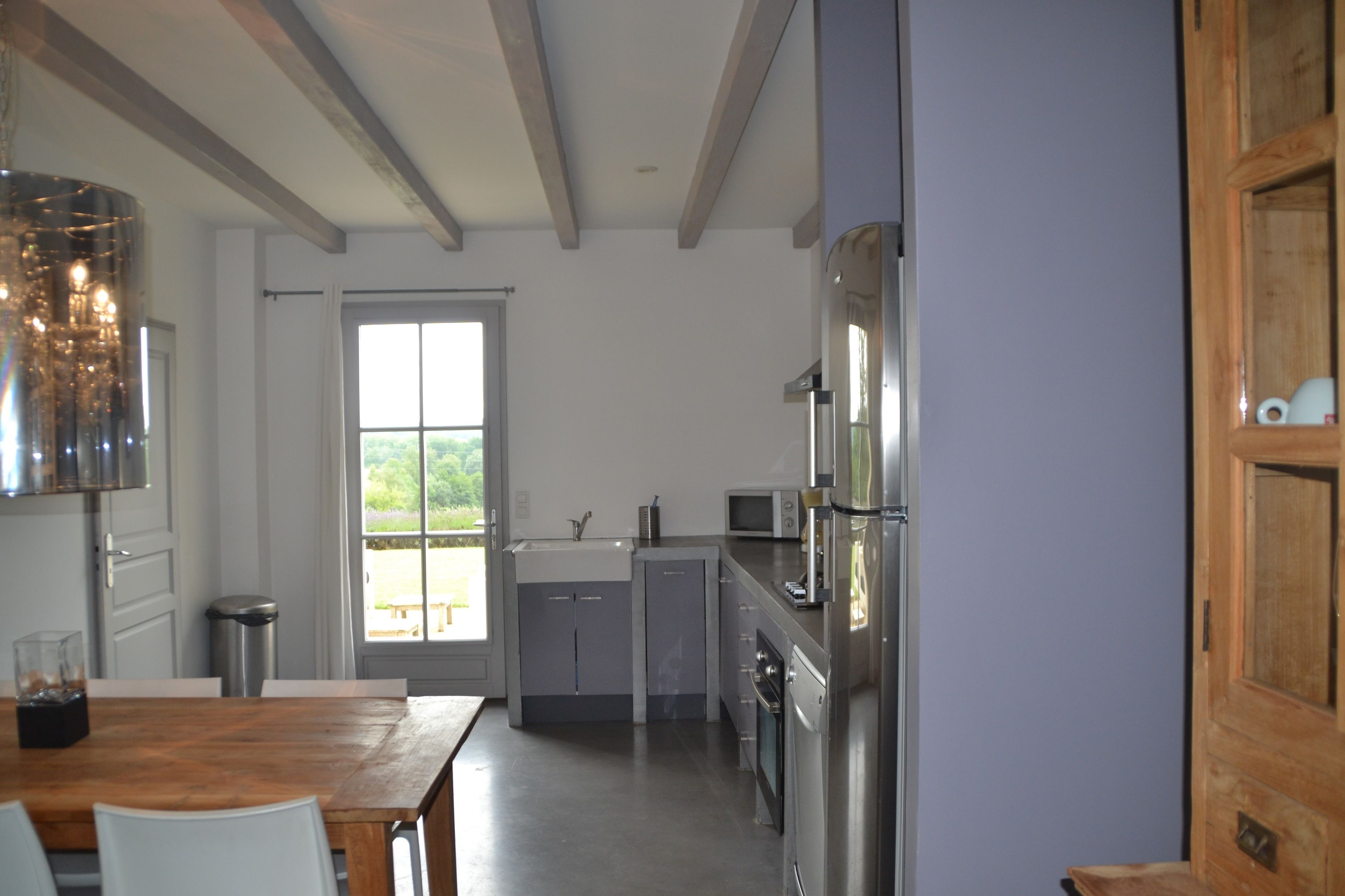 A modern kitchen with a wooden dining table, stainless steel appliances, and a view of the outdoors.