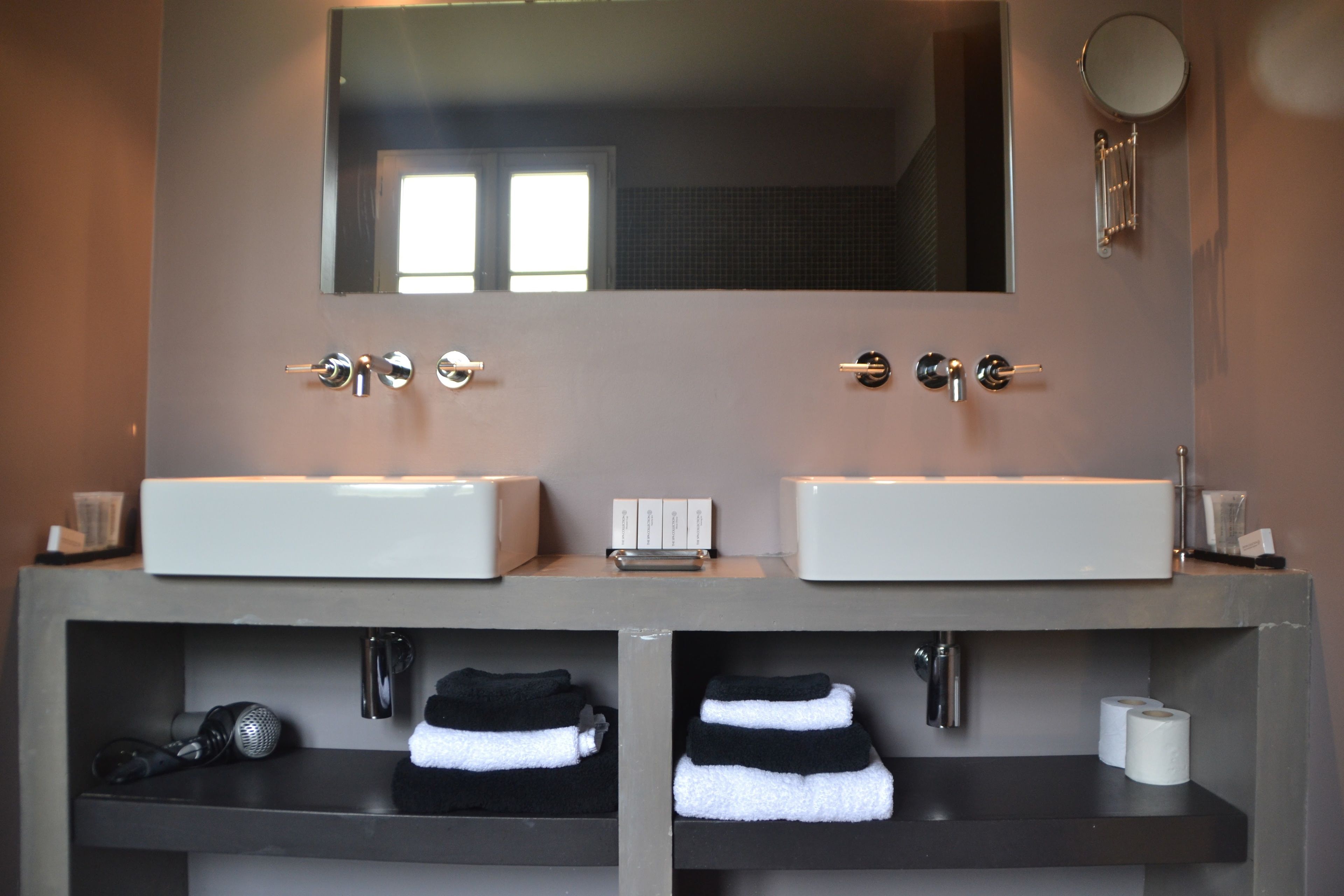 A bathroom with two sinks, a mirror, and shelves with towels and toiletries.
