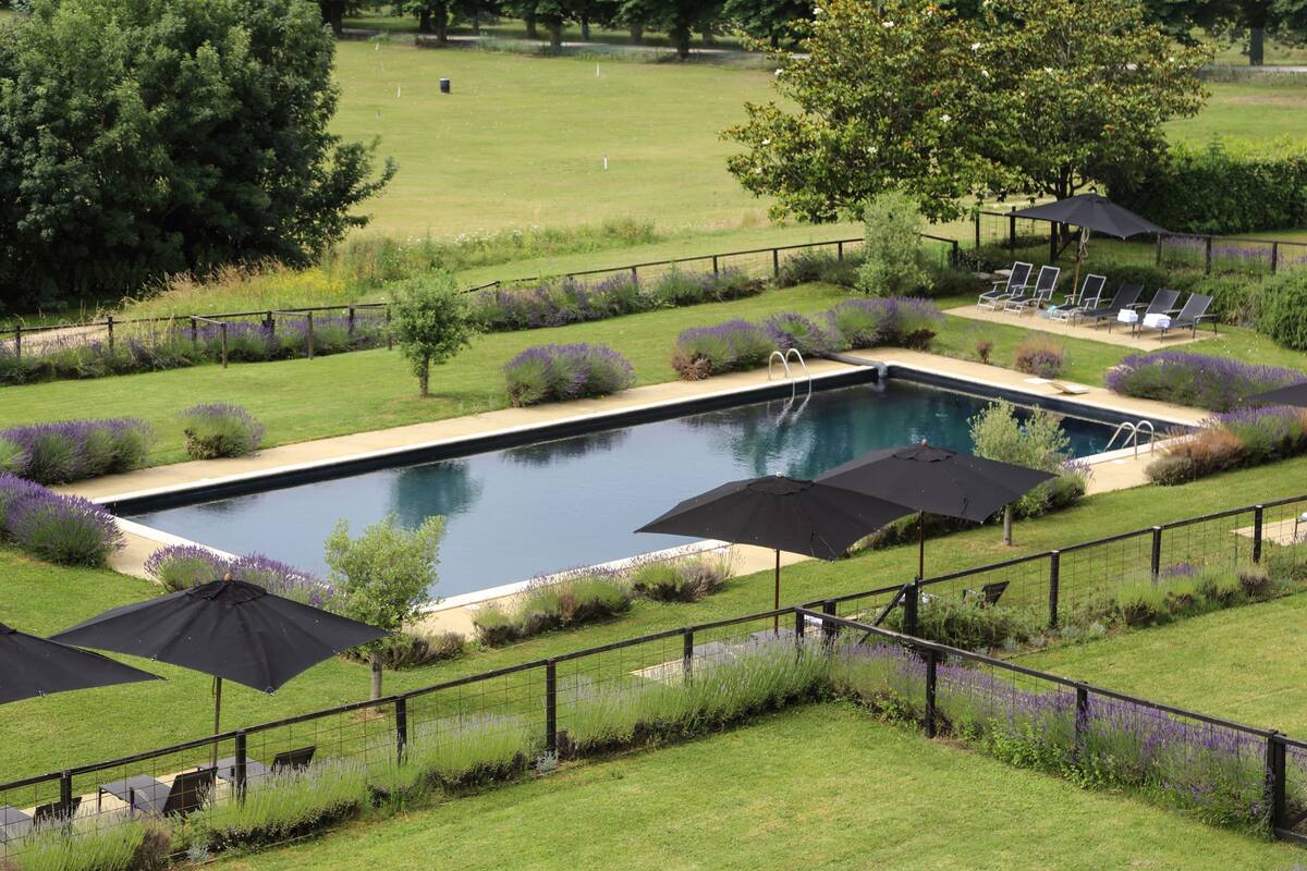 Una piscina rectangular amb un solàrium al voltant, una tanca i diverses paraigües negres.
