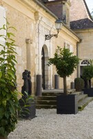 Un edificio de arquitectura clásica, con columnas y arcos, y un pequeño jardín con un árbol y una estatua.