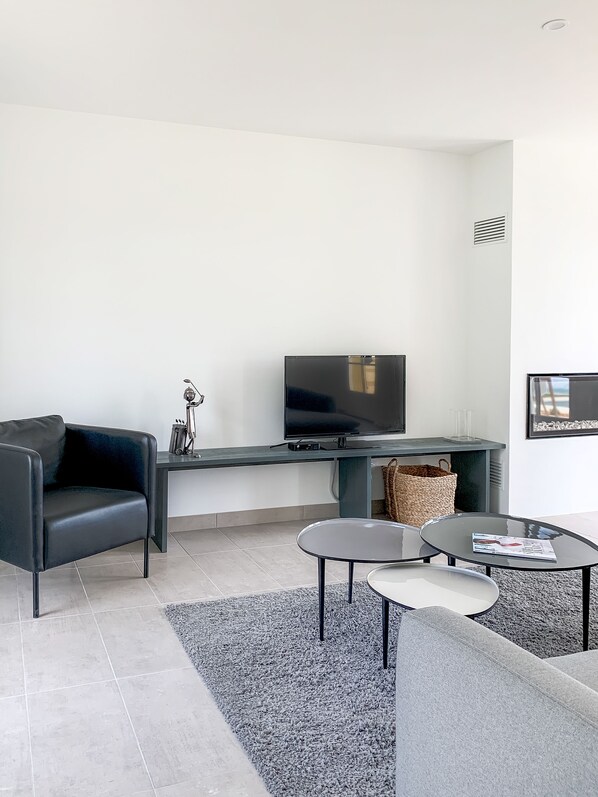A modern living room with a black leather sofa, a flat-screen TV, a small coffee table, and a grey rug.