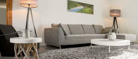A modern living room with a grey sofa, two white coffee tables, and two floor lamps.