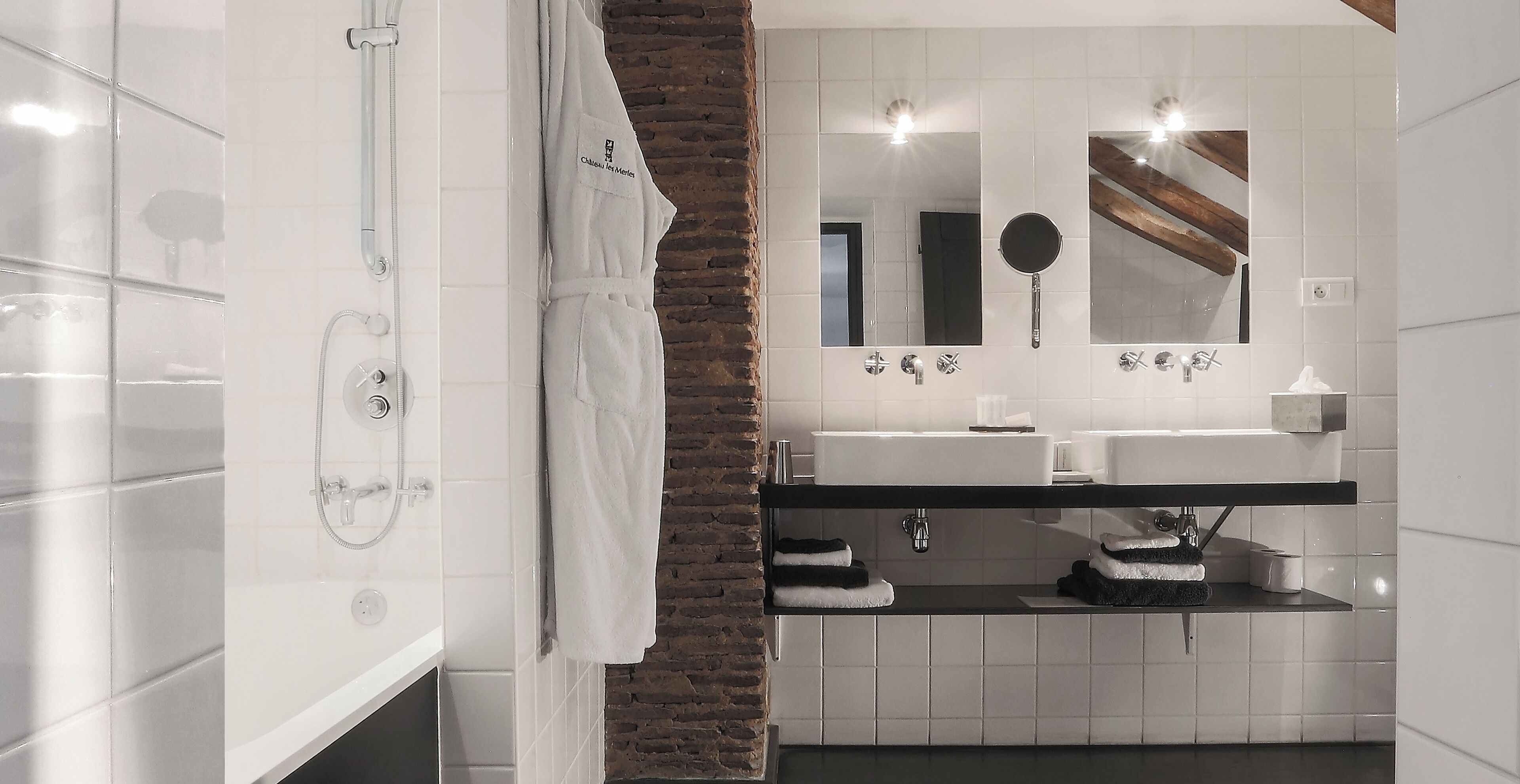 Une salle de bain moderne avec une baignoire blanche, un lavabo sur plan noir et un miroir surmonté d’un autre miroir rond.