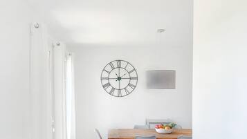 Un comedor con una mesa de madera, sillas grises, un reloj en la pared y una cortina blanca.