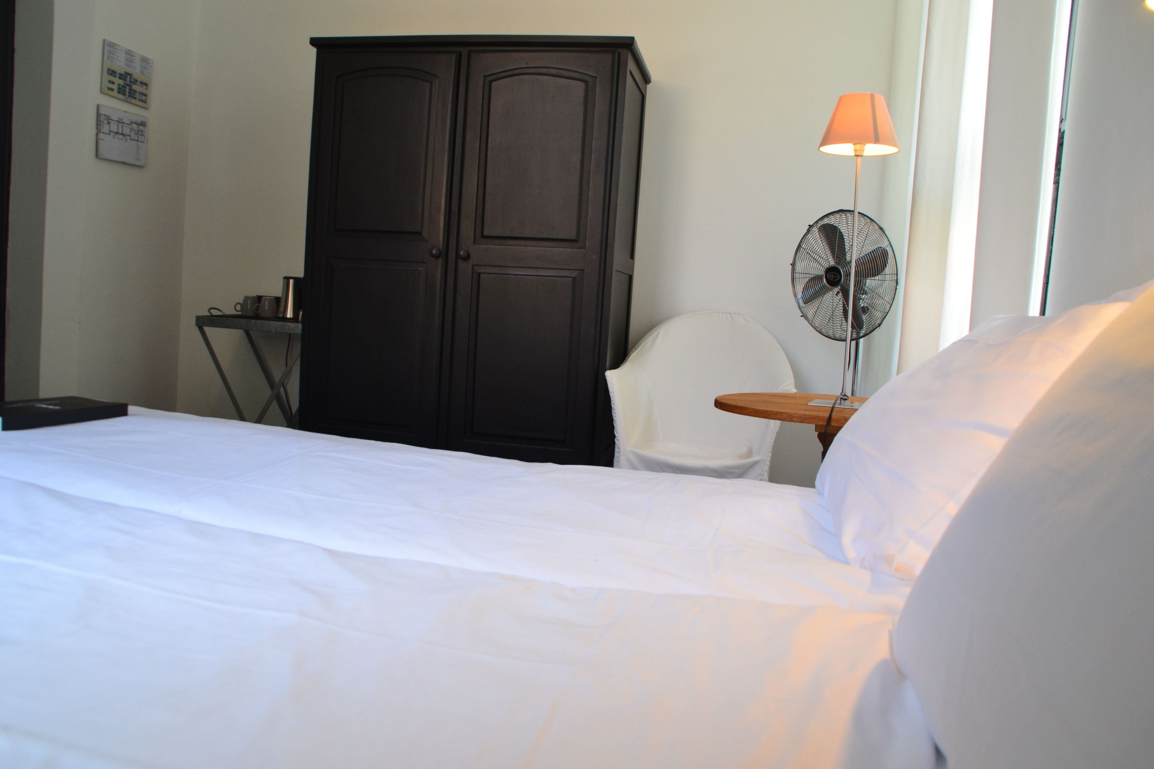 Une chambre d’hôtel comprenant un lit, une armoire, un bureau, une chaise et un ventilateur sur pied.