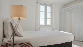 A bedroom with a bed, a bedside lamp, a window, and a wardrobe.