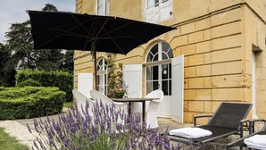 En terrasse med et bord, stole, en parasol og en række lavendelplanter.