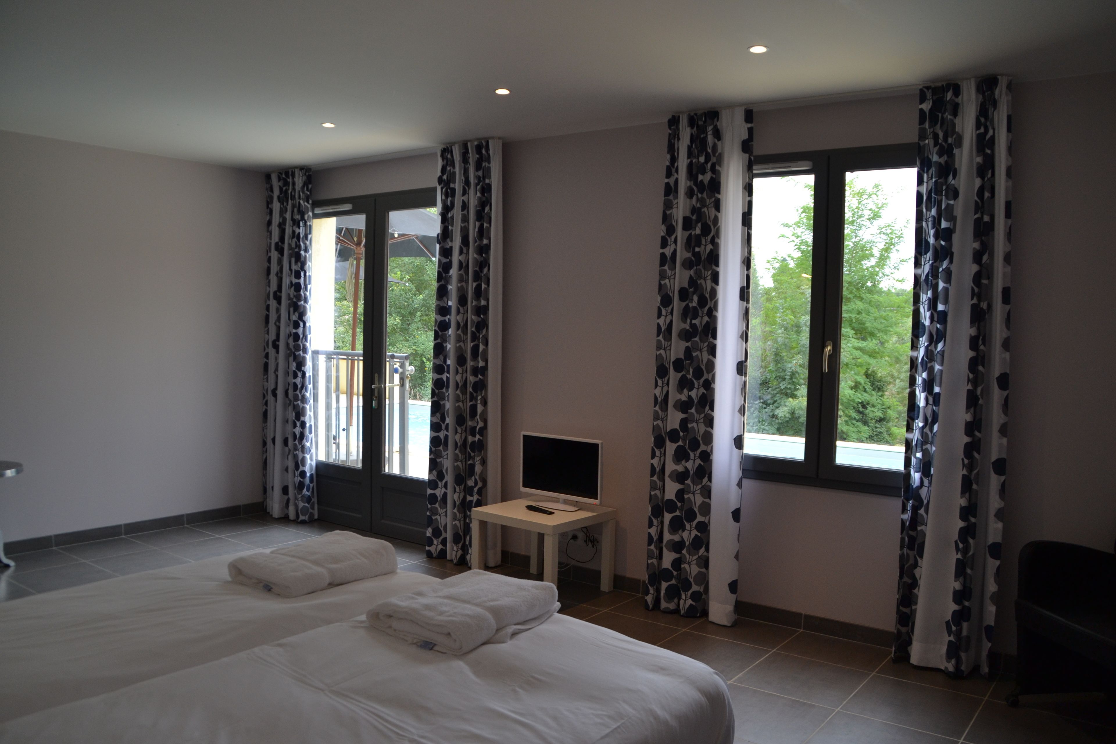 Una habitación de hotel con una cama grande, un escritorio con televisor y cortinas con estampado de hojas.