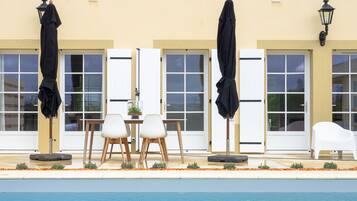 A poolside area with a table and chairs, umbrellas, and a white chair.