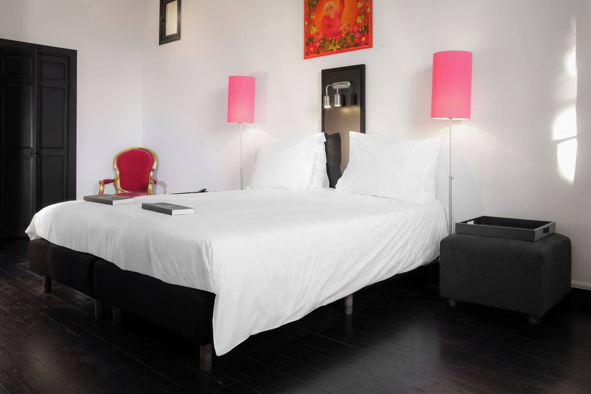 Habitació d'hotel moderna amb un llit gran, un butacó vermell, dues làmpades de nit i una taula petita.