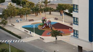 Playful fun awaits at this resort's vibrant playground, featuring a colorful play structure with slides and climbing elements, surrounded by a paved area with benches and a small water feature.