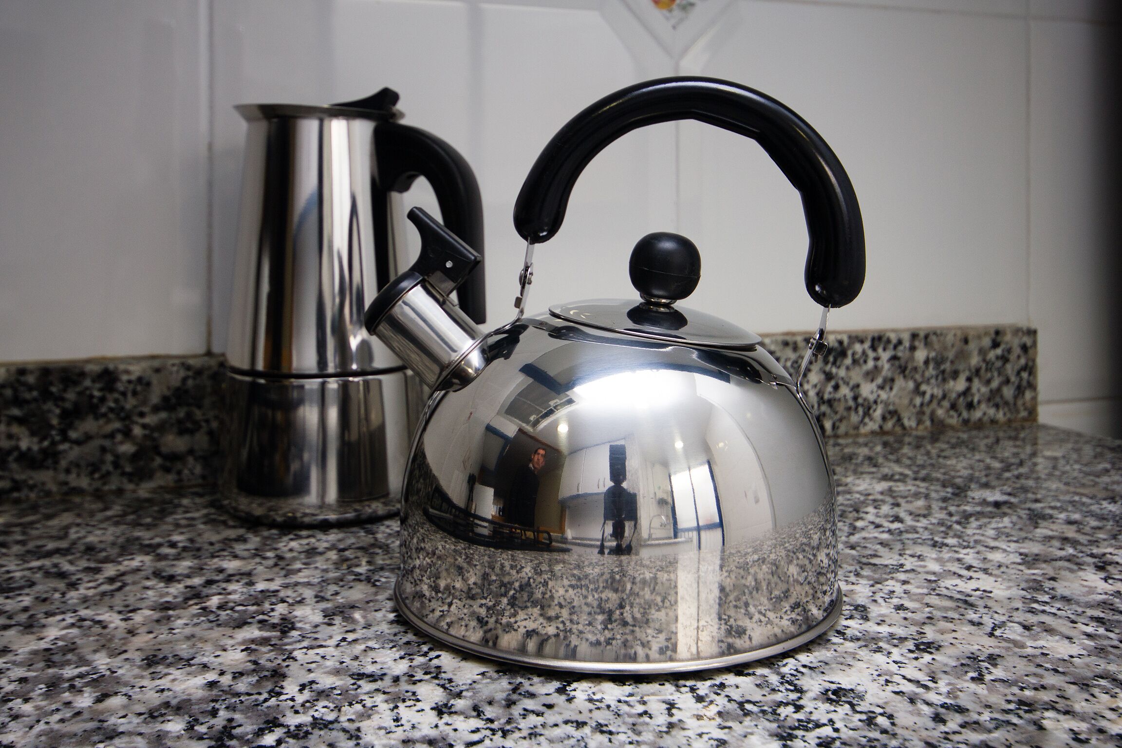 Una tetera de acero inoxidable con asa negra sobre una encimera de granito.