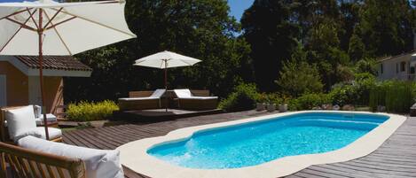 A swimming pool with a wooden deck, lounge chairs, and umbrellas.