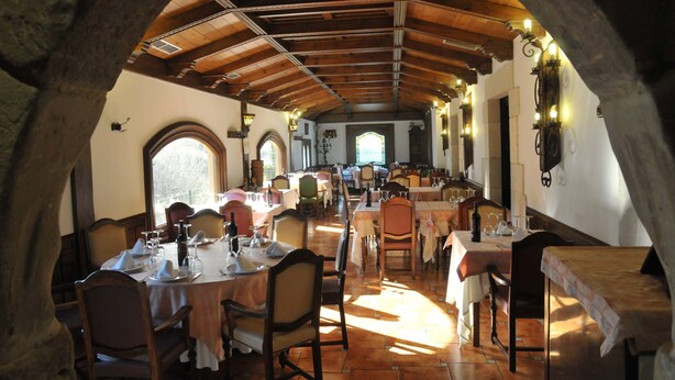 An interior view of a restaurant with wooden beams, tables set for dining, and a view through an arched doorway.