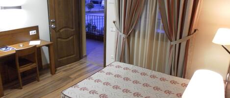 Habitación de hotel con cama, escritorio, silla y puerta que da a un balcón.