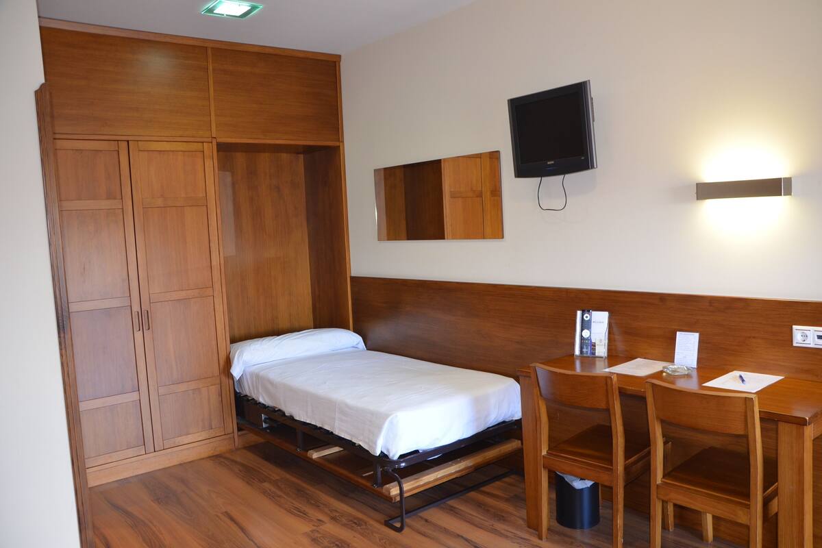 A compact room with a single bed, a desk, and a TV.