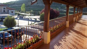 A covered outdoor area with a wooden railing, potted plants, and a view of a building and parked cars.