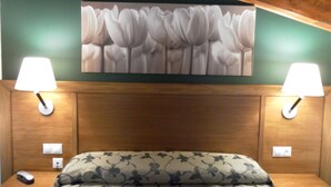 A hotel room with a bed, two bedside lamps, a wall-mounted painting of flowers, and a wooden headboard.