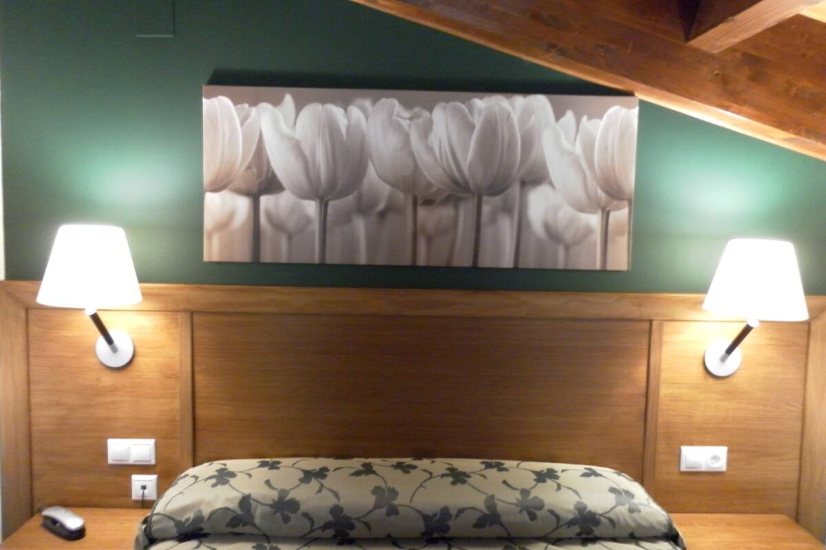 A hotel room with a bed, two bedside lamps, a wall-mounted painting of flowers, and a wooden headboard.