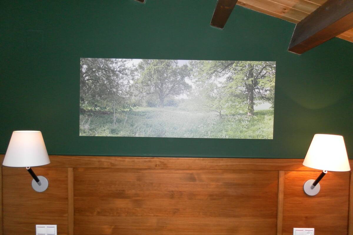 A bedroom with a wooden headboard, two bedside lamps, and a framed picture of a forest path on the wall.