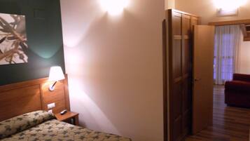 Quarto de hotel com cama, mesa de cabeceira, abajur e porta para outro cômodo.