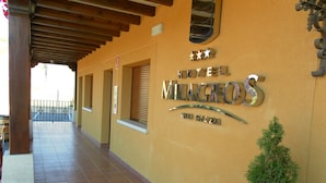 A hotel entrance with a tiled floor, a covered area with wooden beams, and a sign indicating a fire exit.